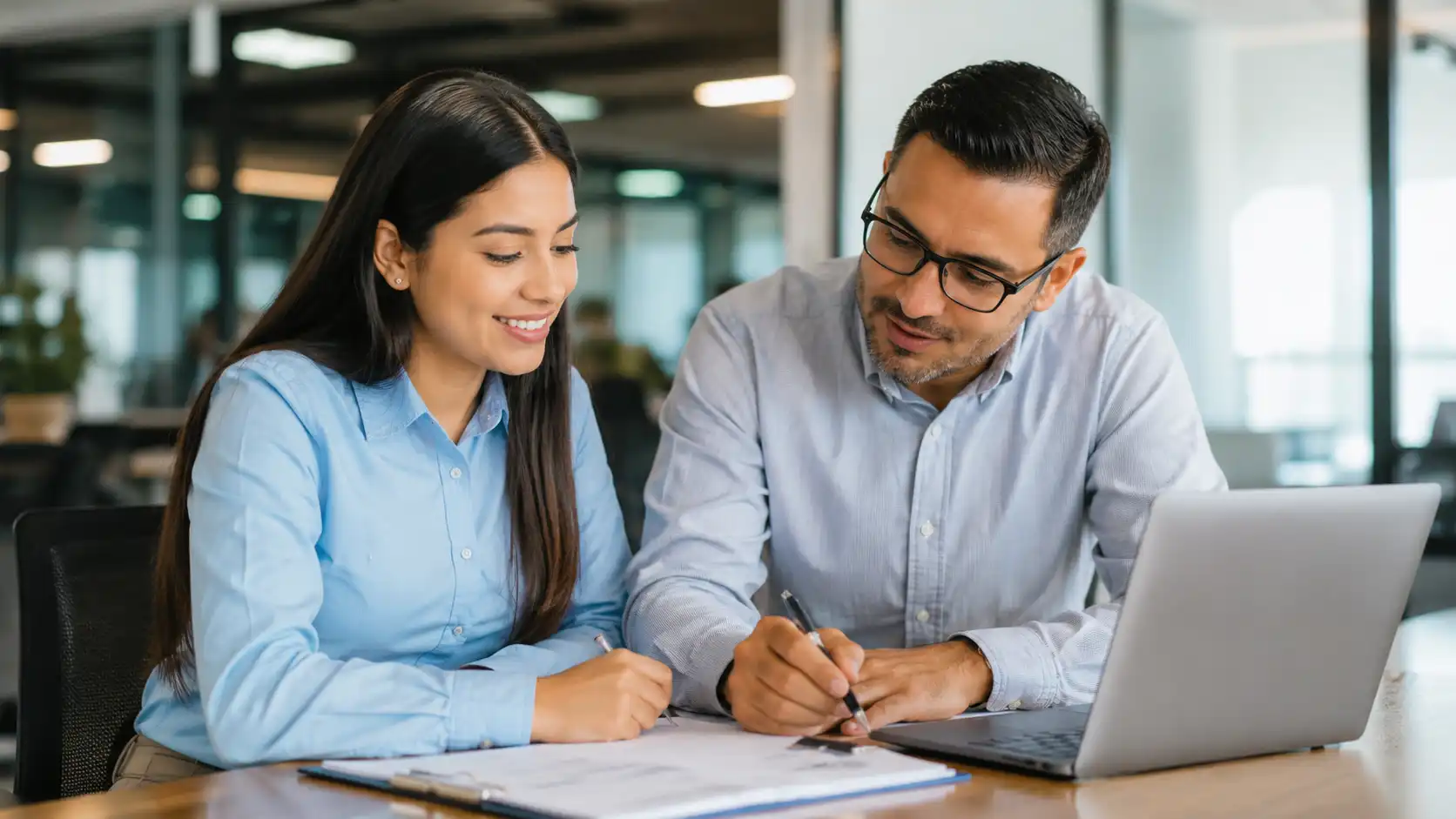 Joven aprendiz colombiano trabajando en una oficina moderna con un mentor durante su contrato de aprendizaje en Colombia